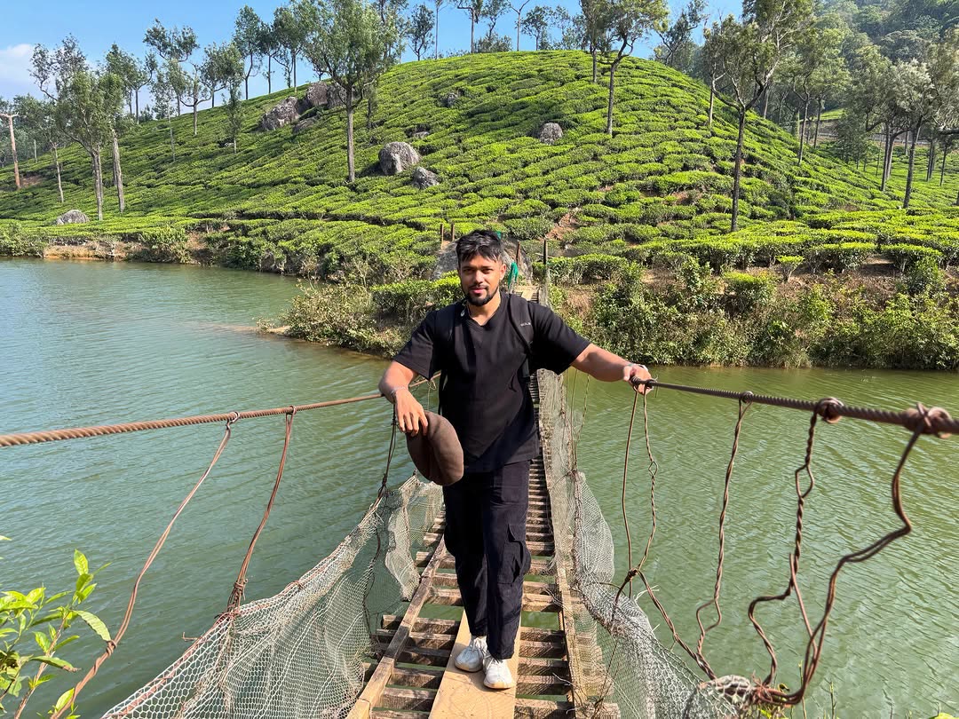 Elio crossing a rope bridge in front of green tea gardens.